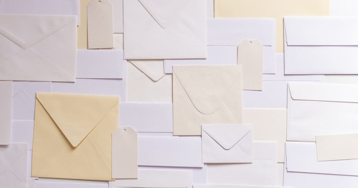 Many pale envelopes in an overlapping grid with one kraft envelope resting on top